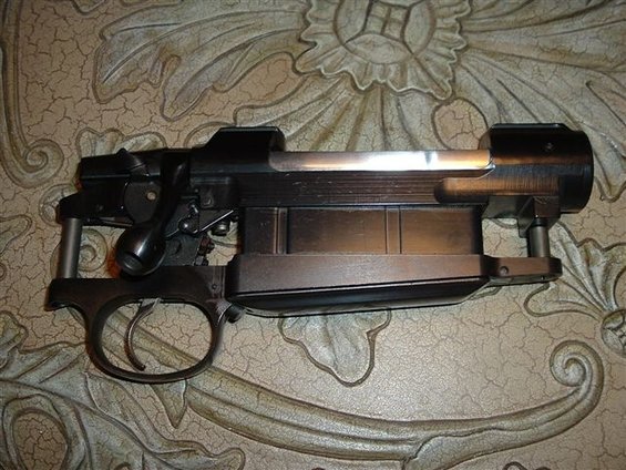 Close-up of a rifle's receiver and trigger assembly, resting on a patterned surface