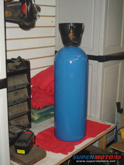 Blue gas cylinder on a red cloth on a workbench, with tools and cabinets in the background