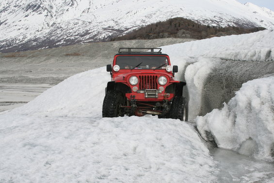 Red Jeep CJ driving through snow and ice with mountains in background