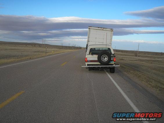 1990 Ford Bronco towing a white box trailer on a highway