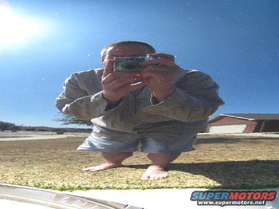 Man in shorts and shirt takes a selfie with a camera, reflected in a shiny surface