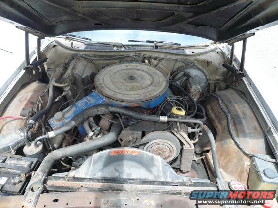 Engine bay of a Ford vehicle, showing the V8 engine, air cleaner, radiator, and battery