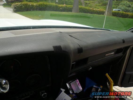 Dashboard of a car with a cracked dash pad and velcro patches. A yellow funnel and other items are in the passenger footwell