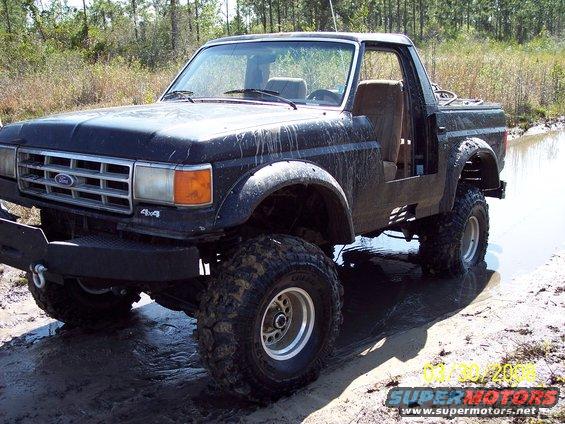 Black Ford Bronco II with lifted suspension and off-road tires stuck in mud