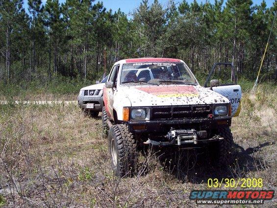 Muddy pickup truck with winch and another SUV behind it in a wooded area
