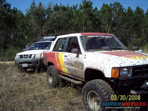 Mud-splattered white 1984 Toyota 4Runner with red, yellow, and orange stripes on the side, parked off-road