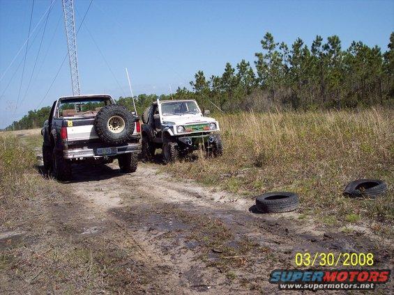Two off-road vehicles on a dirt track with a tower in the background