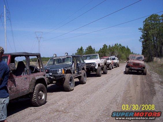 Several lifted Jeeps and trucks parked on a dirt road, with power lines overhead