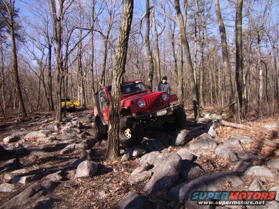 Red 2003 Jeep Wrangler navigating a rocky off-road trail with a yellow Jeep in the background