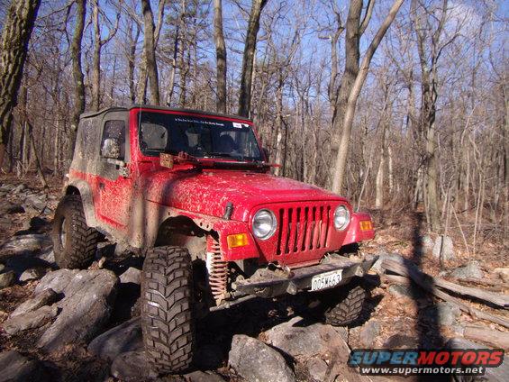 Red 2003 Jeep Wrangler on rocks, mud-splattered, soft top, front grille visible