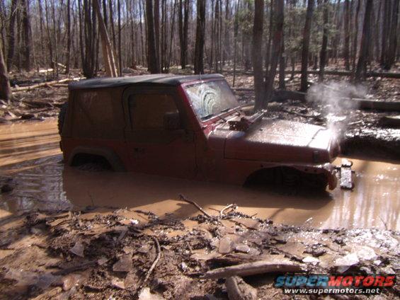 Red 2003 Jeep Wrangler stuck deep in mud with steam rising from the engine