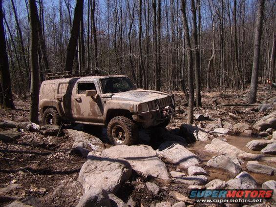 Muddy Hummer H3 off-roading over rocks and water