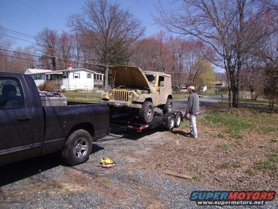 Yellow 2003 Jeep Wrangler on trailer, hood up. Black pickup truck in foreground
