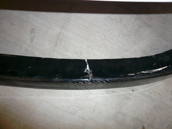 Black curved trim piece with a large crack and visible carbon fiber weave underneath