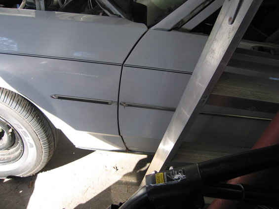 White car fender and door with chrome trim, partially obscured by a ladder