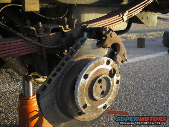 Close-up of a vehicle's brake rotor, caliper, and leaf spring suspension system