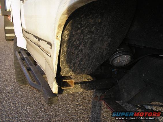 Close-up of a white vehicle's side panel, showing a running board and wheel well. A Supermotors logo is visible at the bottom