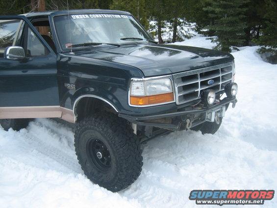 Dark green Ford Bronco with tan lower trim, lifted suspension, and aftermarket bumper in snow
