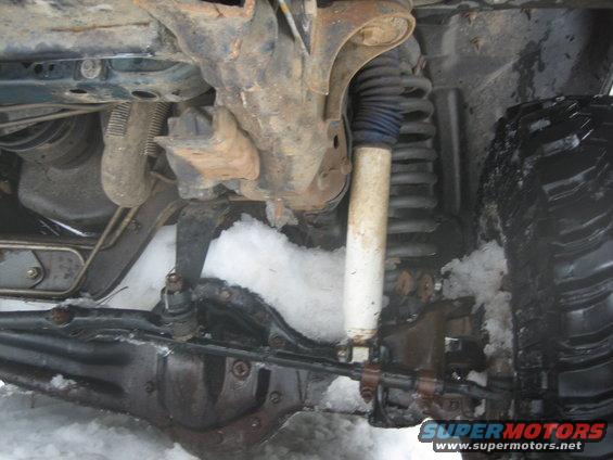 Close-up of a vehicle's front suspension, shock absorber, and tire in snow