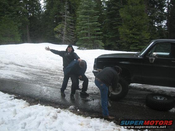 Black 1995 Ford Bronco side view, people changing tire in snow