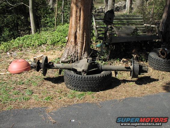 vehicle axle assembly sitting on a tire outdoors next to a tree and a wooden bench