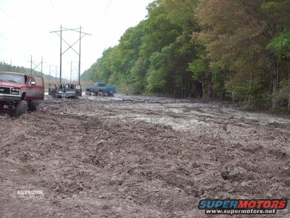 Muddy scene with red GMC truck and blue Ford truck stuck in mud
