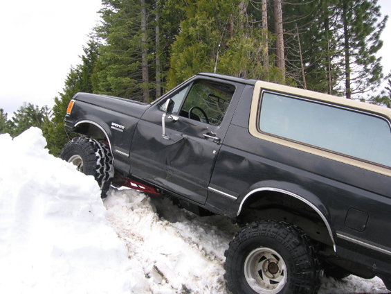 Dark gray Ford Bronco with a tan top stuck in snow, dented driver's side door