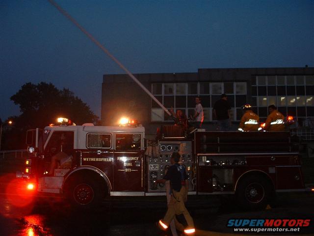 Fire truck with flashing lights and a water stream at dusk