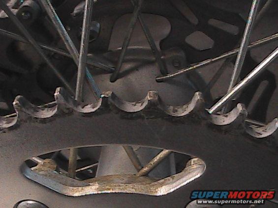 Motorcycle rear sprocket with spokes visible, showing wear on teeth