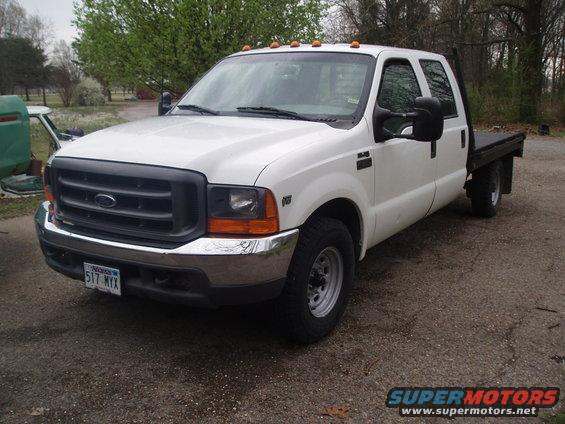White 1999 Ford F-350 flatbed truck, front 3/4 view, parked on gravel