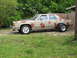 1985 Ford Crown Victoria LTD - A tan sedan with a black hood and red spray-painted shapes is parked on a grassy area.