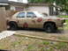 1985 Ford Crown Victoria LTD - A tan sedan with a black hood and red splotches on its body is parked in a grassy area.