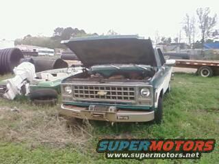 1977 Chevrolet pickup truck, green and white, hood open, parked in a grassy lot with debris