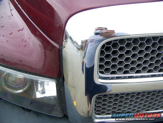 Red truck's front grille with honeycomb pattern and headlight. Reflection shows a person holding a camera