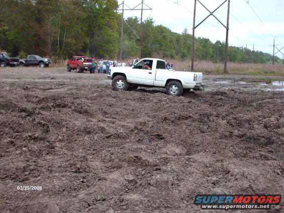 White pickup truck with lifted suspension driving through mud. The truck has a single cab and short bed