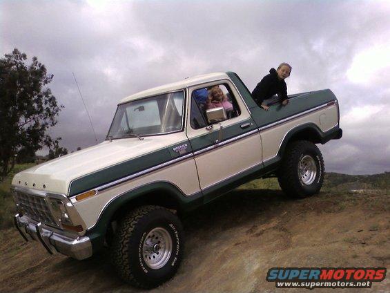 1978 Ford Bronco, cream and green, with children in cab and bed, parked on a dirt incline