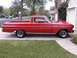 1965 Ford Ranchero - A red 1965 Ford Ranchero is parked in front of a garage, showing its side profile with custom wheels.