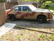1985 Ford Crown Victoria LTD - A tan sedan with a crude red camouflage paint job sits in a yard next to a wooden fence.