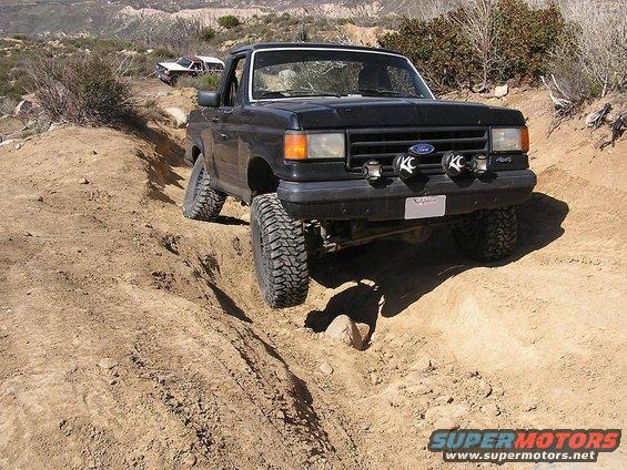 Black 1990 Ford Bronco navigating a steep dirt trail with another vehicle visible in the background