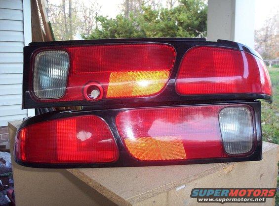 Two red car taillights with amber turn signals and clear reverse lights, stacked on a wooden surface