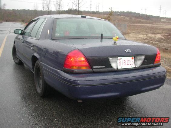 Dark blue sedan parked on a wet road. Has a yellow rubber duck on the trunk