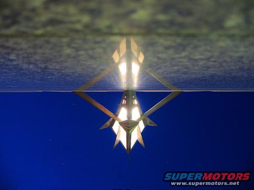Geometric light fixture with illuminated panels against a blue background, reflection visible