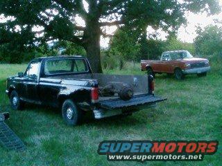 Black 1987 Ford F-150 pickup truck with tailgate down, parked in grassy field next to a red pickup truck