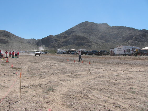 Off-road race event with multiple vehicles, trailers, and spectators in a desert landscape