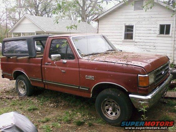 Maroon 1987 Ford F-150 pickup truck with a black camper shell parked in a yard