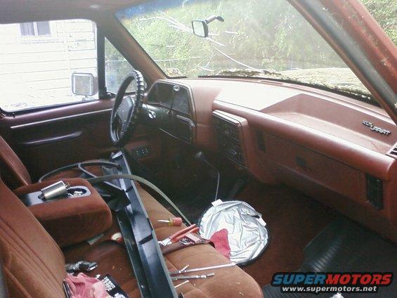 1987 Ford F-150 interior with brown upholstery, cracked windshield, and tools on the passenger seat