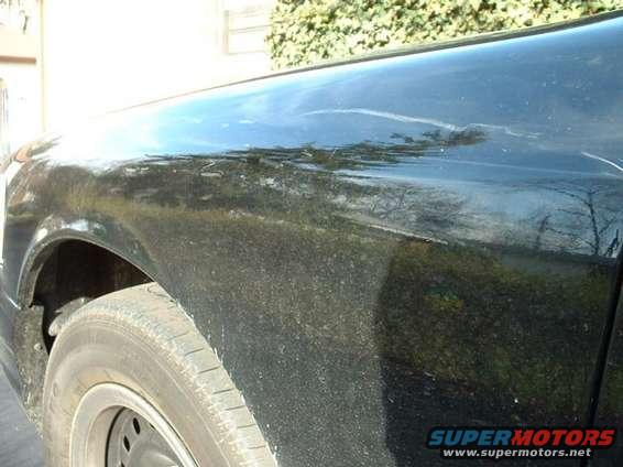 Side view of a black sedan's fender with some damage and dirt. Supermotors.net logo visible