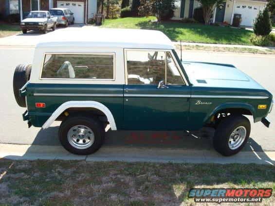 Green 1977 Ford Bronco with white hardtop, spare tire on rear, seen from the side