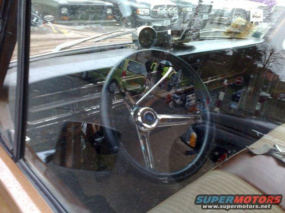 Interior shot of a car, showing the steering wheel and dashboard. Reflections in the windshield show other vehicles