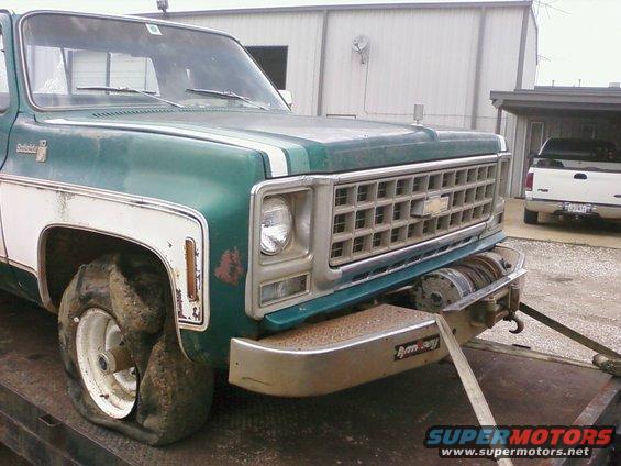 Green Chevrolet pickup truck with flat tire, winch on front bumper. White pickup truck in background. 1977 model year